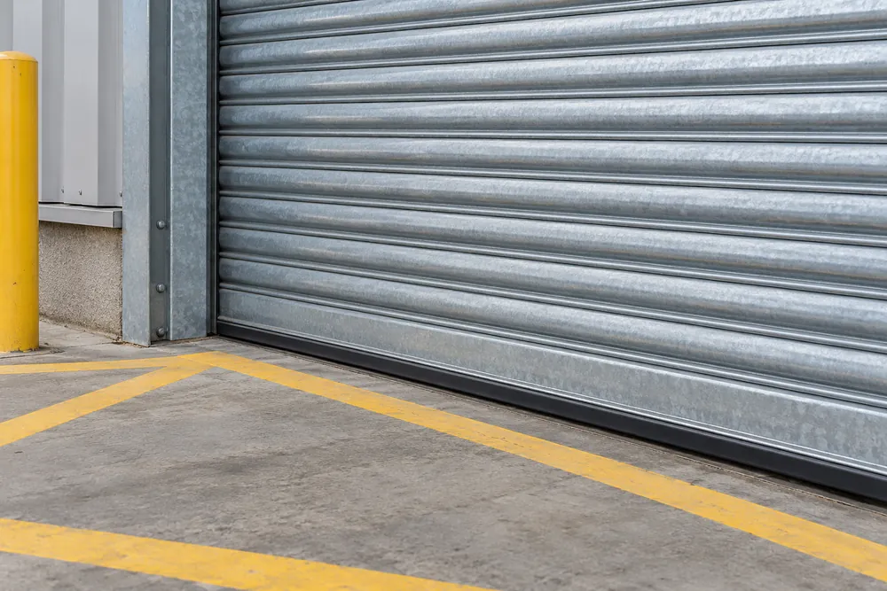 Galvanised shutter curtain and guide rail above a yellow marked warehouse floor